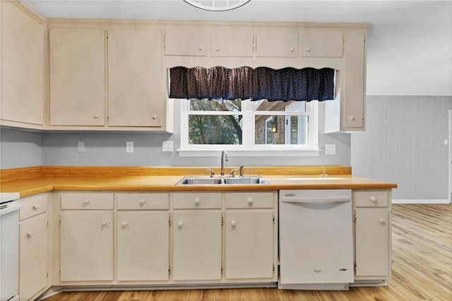 kitchen with cream cabinetry, light countertops, light wood-style flooring, white dishwasher, and a sink