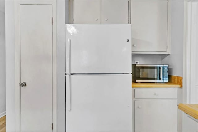 kitchen with stainless steel microwave, freestanding refrigerator, and white cabinetry