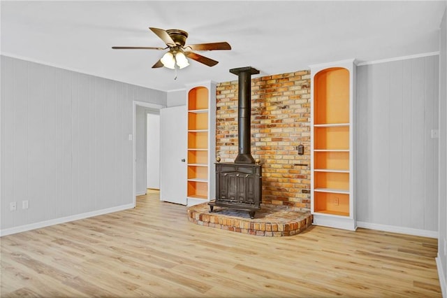 unfurnished living room featuring baseboards, built in features, ornamental molding, wood finished floors, and a wood stove