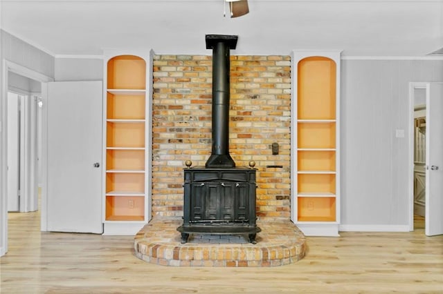 interior details with a wood stove, built in features, crown molding, and wood finished floors