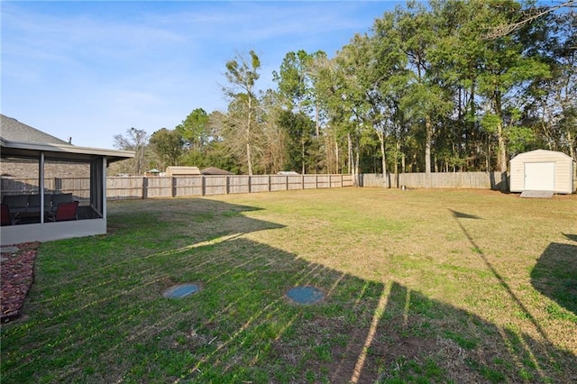 view of yard featuring an outbuilding, a storage unit, a fenced backyard, and a sunroom