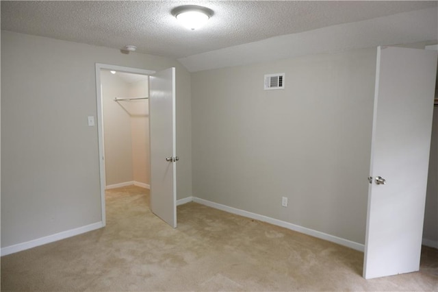 unfurnished bedroom with a textured ceiling, a walk in closet, light carpet, and a closet