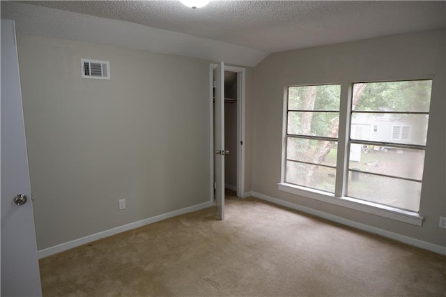 unfurnished bedroom with light carpet, a textured ceiling, vaulted ceiling, and a closet