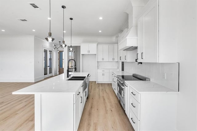 kitchen with light wood-type flooring, light stone counters, decorative backsplash, pendant lighting, and a spacious island