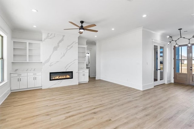 unfurnished living room with crown molding, light wood-type flooring, built in shelves, ceiling fan, and a premium fireplace