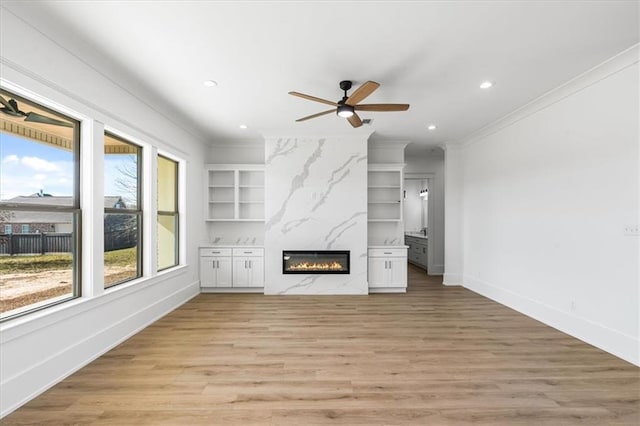 unfurnished living room featuring a premium fireplace, ceiling fan, built in features, ornamental molding, and light hardwood / wood-style flooring