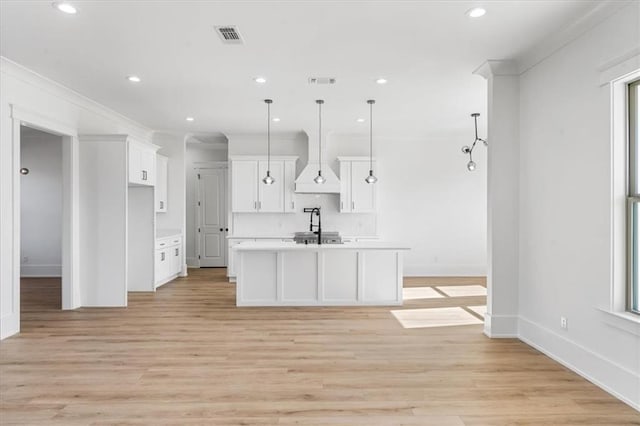 kitchen with white cabinets, pendant lighting, light hardwood / wood-style floors, custom exhaust hood, and an island with sink