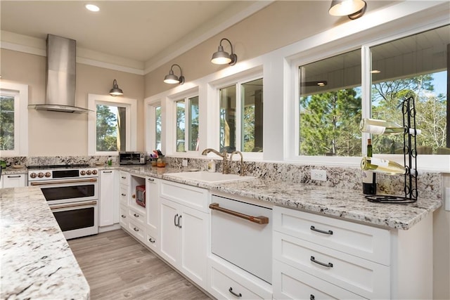 kitchen with range with two ovens, ornamental molding, white cabinets, a sink, and wall chimney exhaust hood