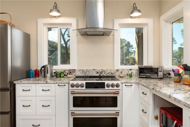 kitchen with a toaster, range with two ovens, freestanding refrigerator, wall chimney range hood, and white cabinetry