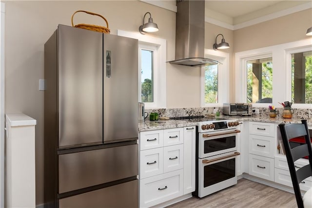 kitchen with island exhaust hood, freestanding refrigerator, white cabinetry, light stone countertops, and double oven range