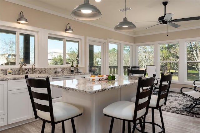 kitchen with a healthy amount of sunlight, white cabinetry, visible vents, and crown molding