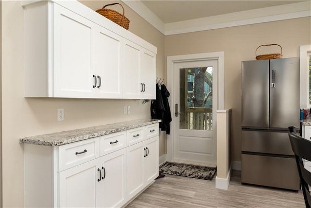 kitchen with light wood-type flooring, light stone countertops, freestanding refrigerator, and white cabinetry