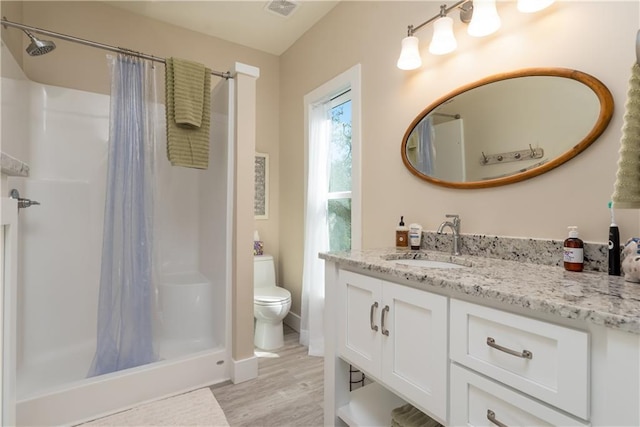 full bathroom featuring a stall shower, visible vents, toilet, wood finished floors, and vanity