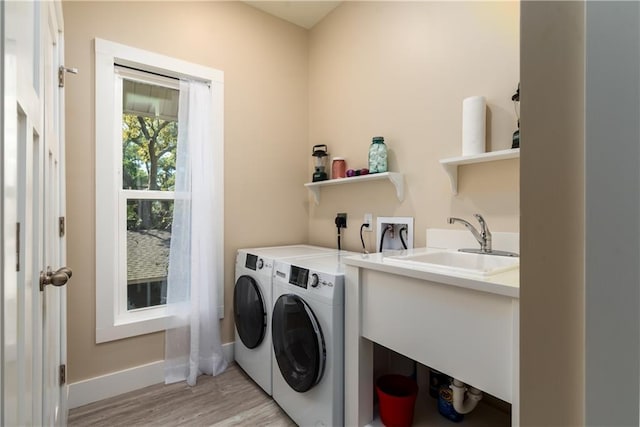 laundry area with laundry area, light wood finished floors, baseboards, washer and clothes dryer, and a sink