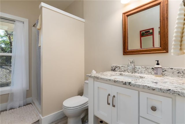 bathroom with toilet, walk in shower, vanity, and baseboards