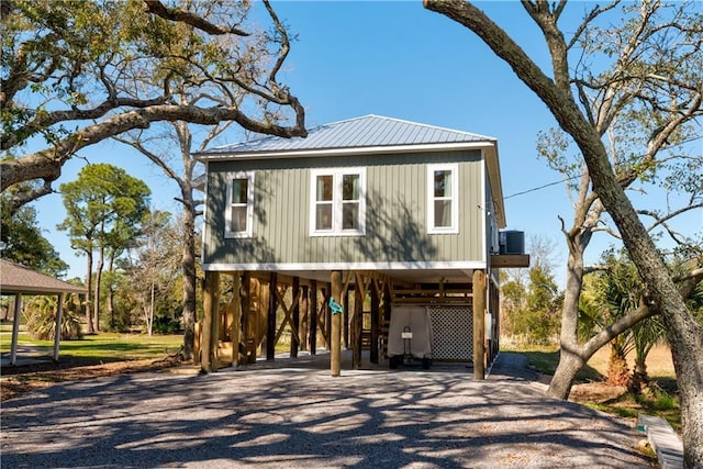 coastal inspired home with gravel driveway, stairs, metal roof, and a carport