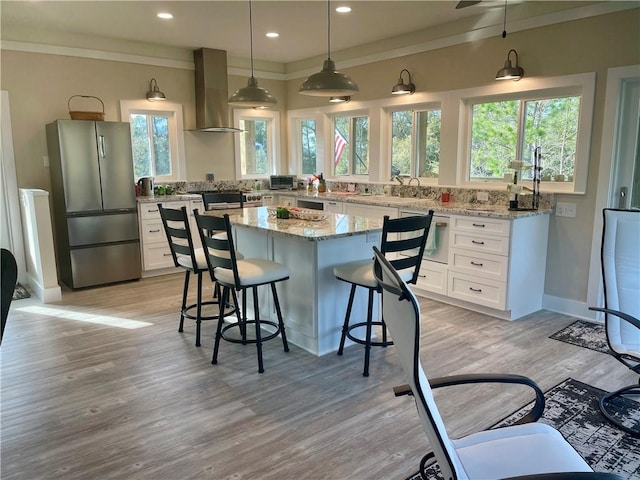 kitchen with light stone counters, a center island, island exhaust hood, freestanding refrigerator, and white cabinetry