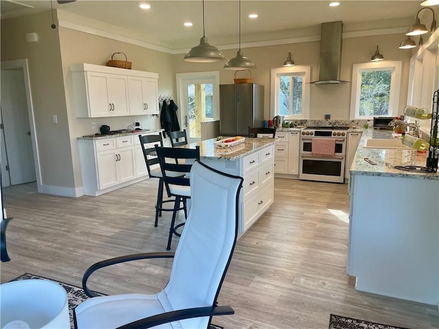 kitchen featuring wall chimney exhaust hood, appliances with stainless steel finishes, light stone counters, crown molding, and a wealth of natural light