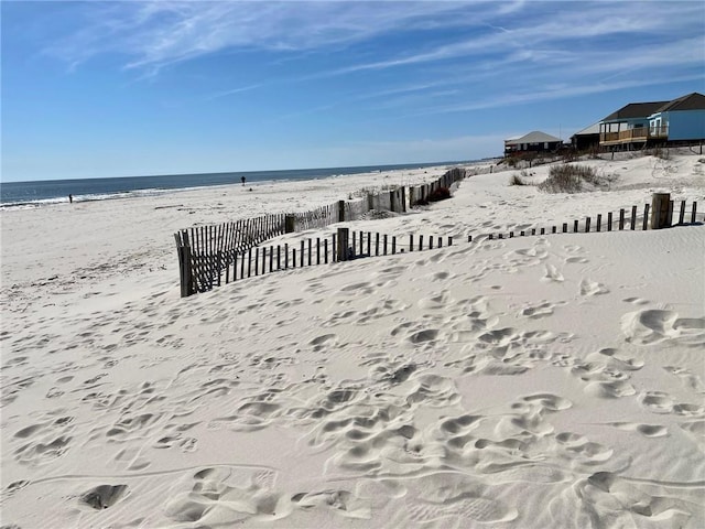 exterior space featuring a view of the beach, a water view, and fence