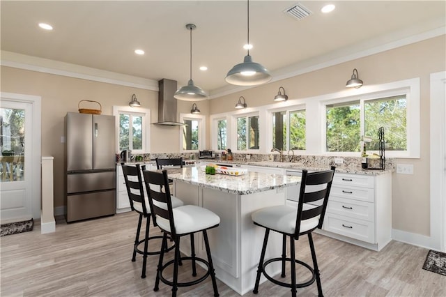 kitchen with visible vents, wall chimney exhaust hood, ornamental molding, a breakfast bar area, and freestanding refrigerator