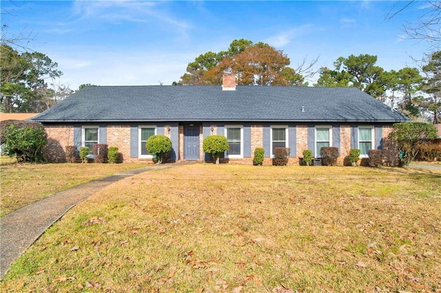 ranch-style house featuring brick siding, a chimney, a front yard, and roof with shingles