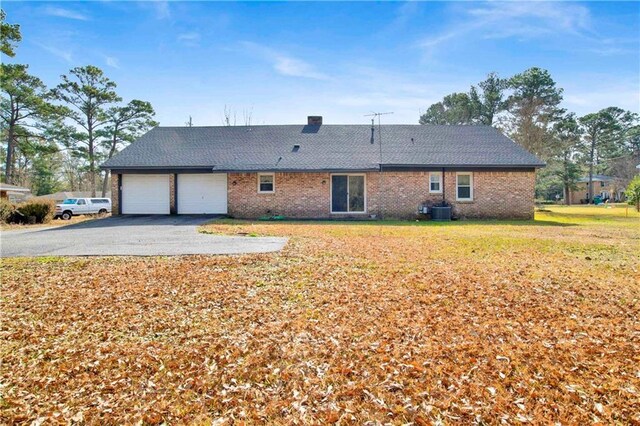 rear view of property featuring aphalt driveway, central air condition unit, a chimney, a yard, and an attached garage