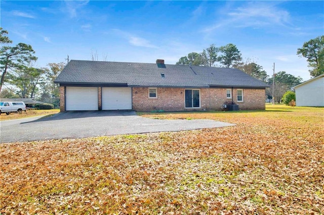 rear view of house featuring driveway, central AC, a yard, a garage, and brick siding