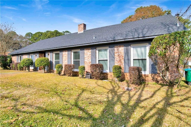 rear view of property featuring a yard, brick siding, roof with shingles, and a chimney