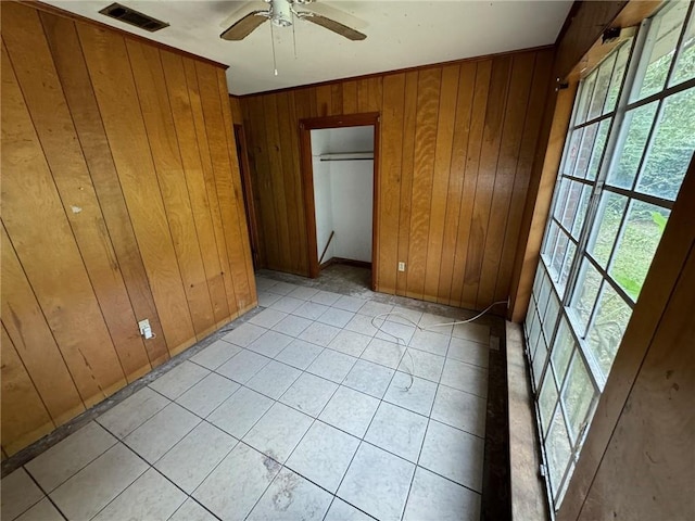 tiled empty room featuring ceiling fan and wood walls