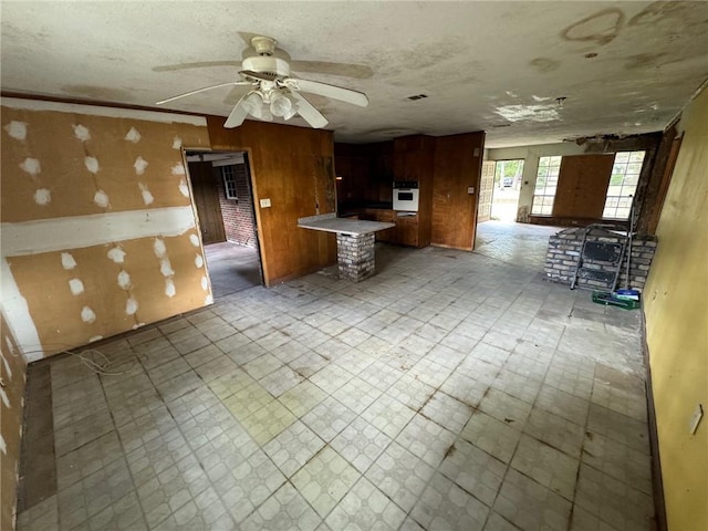 kitchen featuring oven, a textured ceiling, kitchen peninsula, ceiling fan, and wooden walls