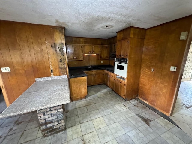 kitchen featuring sink, white oven, a textured ceiling, and wood walls