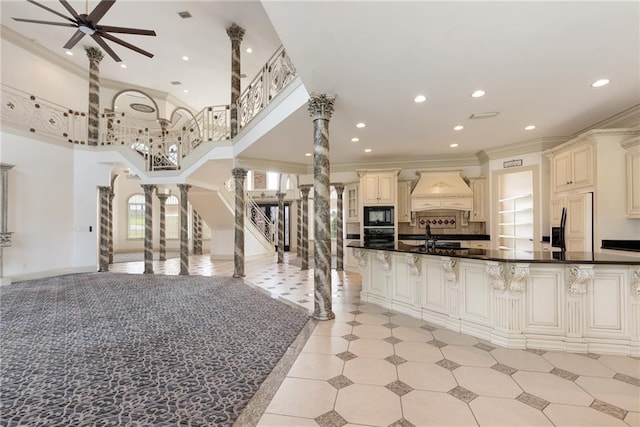 kitchen with built in appliances, open floor plan, cream cabinets, custom range hood, and ornate columns