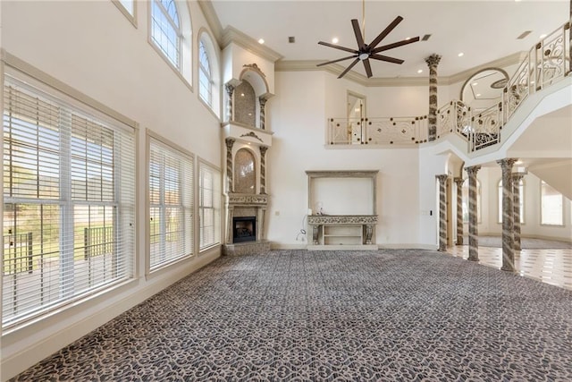 living area featuring carpet, a premium fireplace, a towering ceiling, ornamental molding, and a ceiling fan