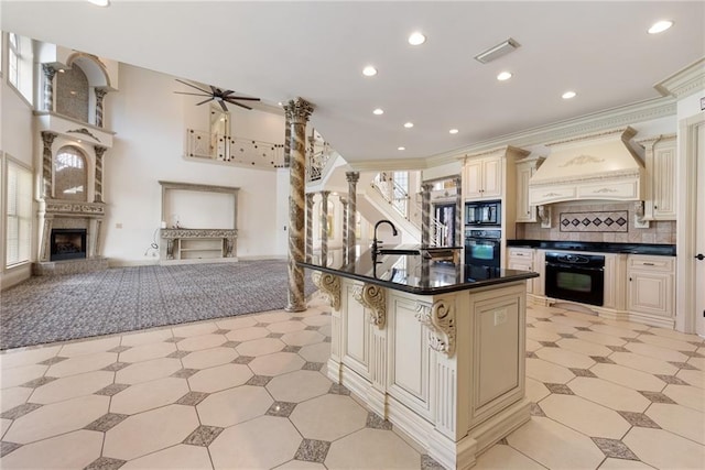 kitchen featuring cream cabinetry, a sink, custom range hood, open floor plan, and black appliances