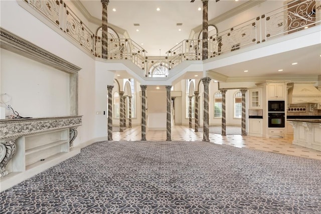 interior space with a towering ceiling, ornamental molding, light carpet, and ornate columns