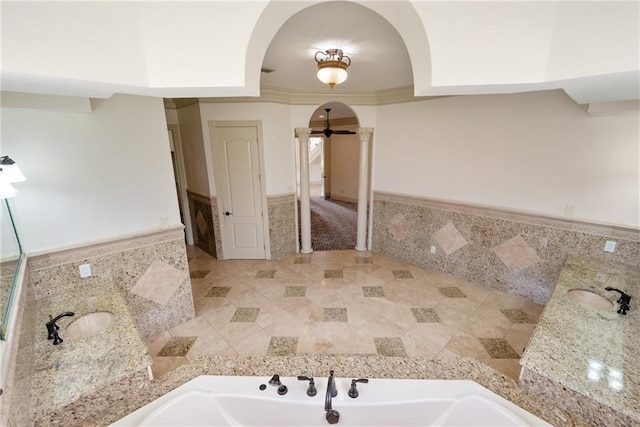 bathroom featuring decorative columns, wainscoting, tile walls, and a bath