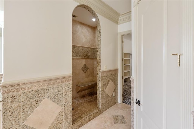 full bath featuring a wainscoted wall, crown molding, a walk in shower, a walk in closet, and tile walls