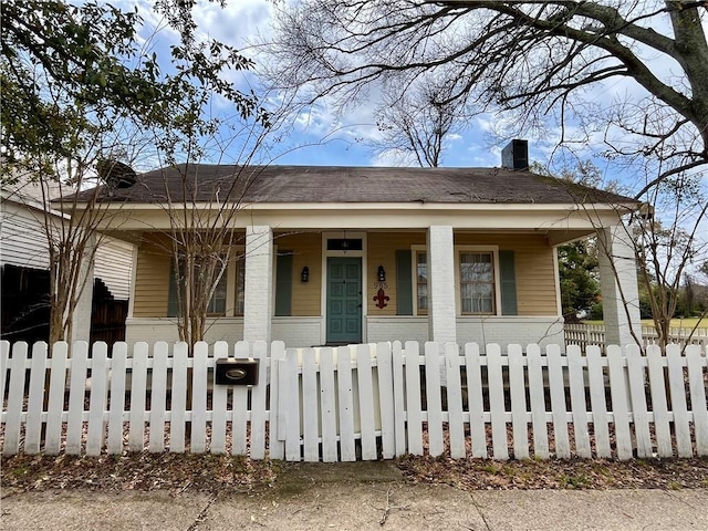 bungalow-style home with a porch, a chimney, brick siding, and a fenced front yard