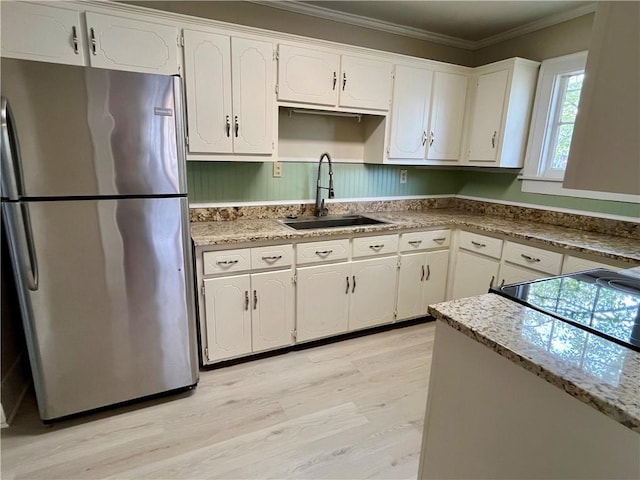 kitchen with white cabinetry, ornamental molding, a sink, and freestanding refrigerator