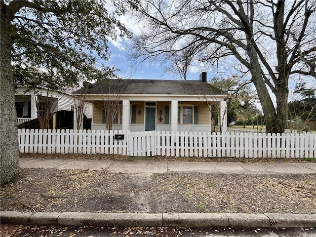 bungalow with covered porch, a fenced front yard, and a chimney