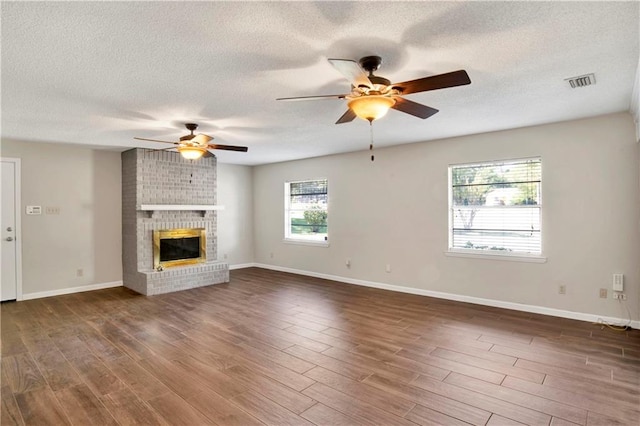 unfurnished living room with dark hardwood / wood-style floors, ceiling fan, a textured ceiling, and a brick fireplace