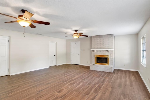 unfurnished living room featuring ceiling fan, wood-type flooring, a textured ceiling, and a brick fireplace