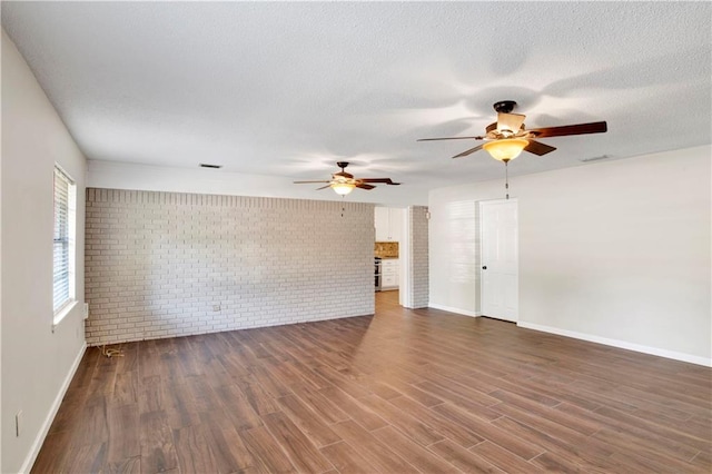 empty room featuring brick wall, a textured ceiling, dark hardwood / wood-style floors, and ceiling fan