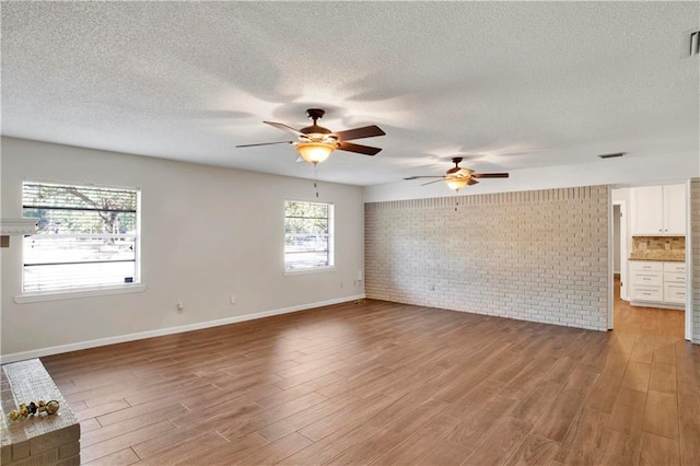 spare room with ceiling fan, brick wall, wood-type flooring, and a textured ceiling