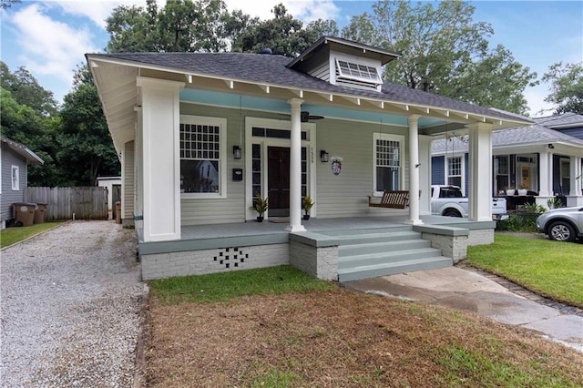 bungalow-style home with a front lawn, roof with shingles, covered porch, and fence