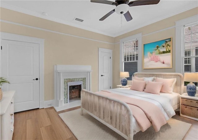 bedroom featuring ceiling fan, visible vents, crown molding, light wood-style floors, and a fireplace
