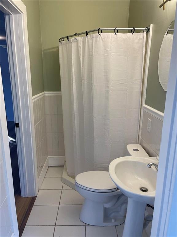 full bathroom featuring a shower with curtain, toilet, wainscoting, a sink, and tile patterned floors