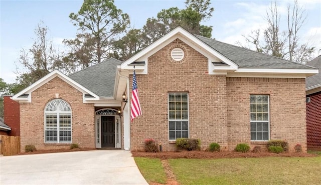 traditional-style home with a front yard, brick siding, and roof with shingles