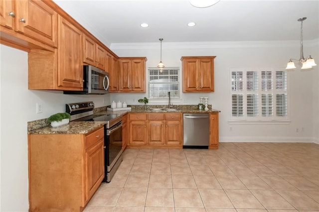 kitchen featuring brown cabinetry, dark stone counters, ornamental molding, a sink, and appliances with stainless steel finishes