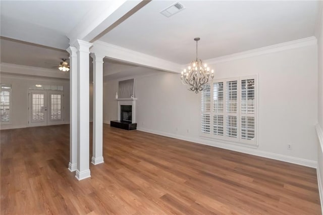 unfurnished dining area with visible vents, a fireplace with raised hearth, ceiling fan with notable chandelier, crown molding, and ornate columns